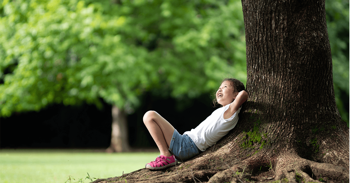 young child laying under large tree in the shade
