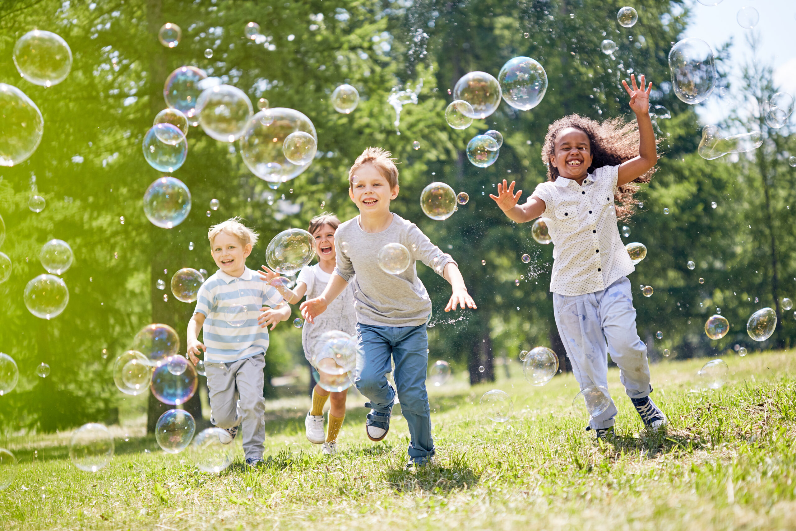 four children running through grass chasing bubbles