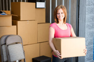A woman holding a large cardboard box, standing in front a storage unit.