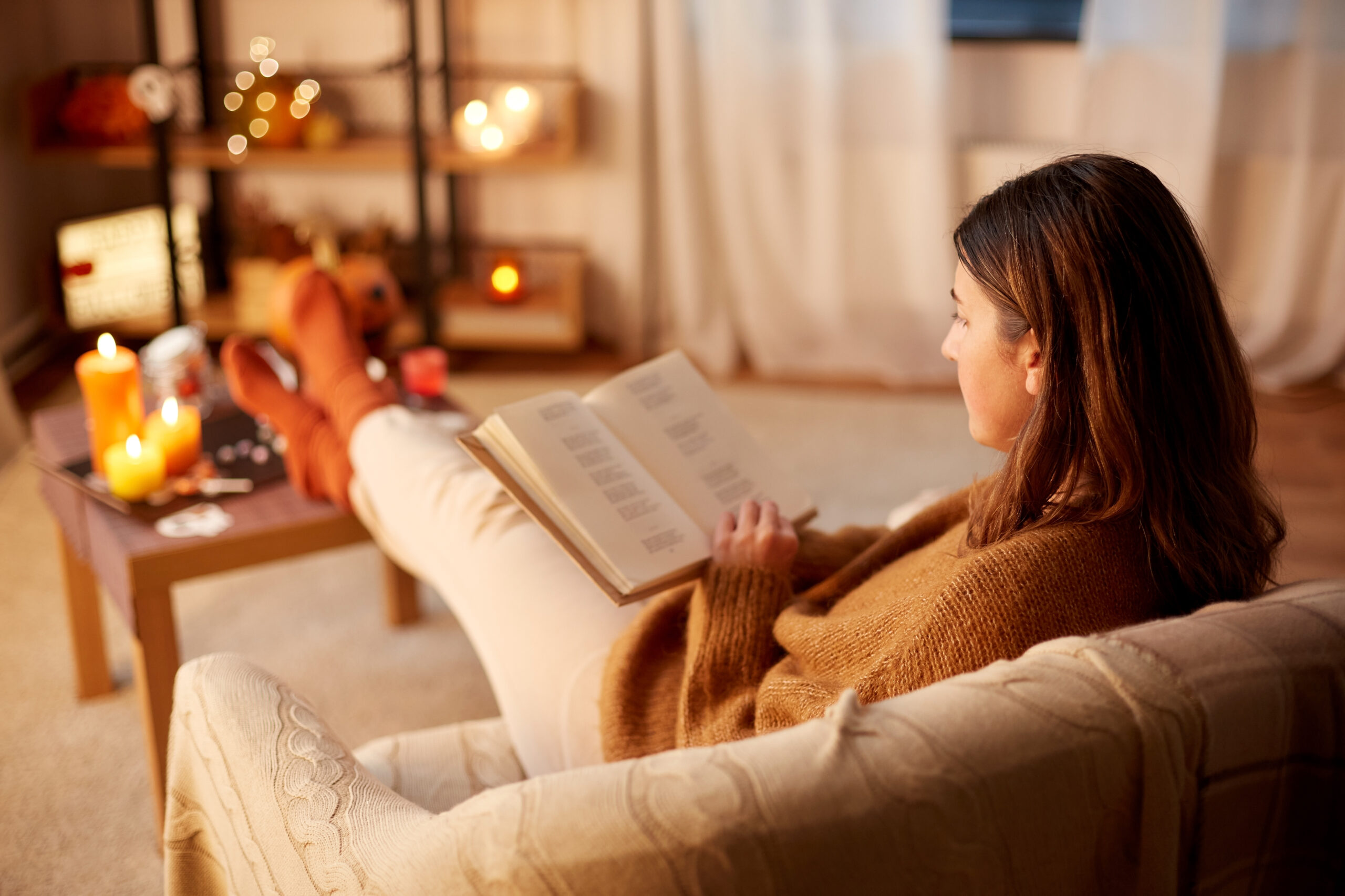 A woman sitting on a sofa reading a book and enjoying the comfort of her clutter free, cosy autumn home.