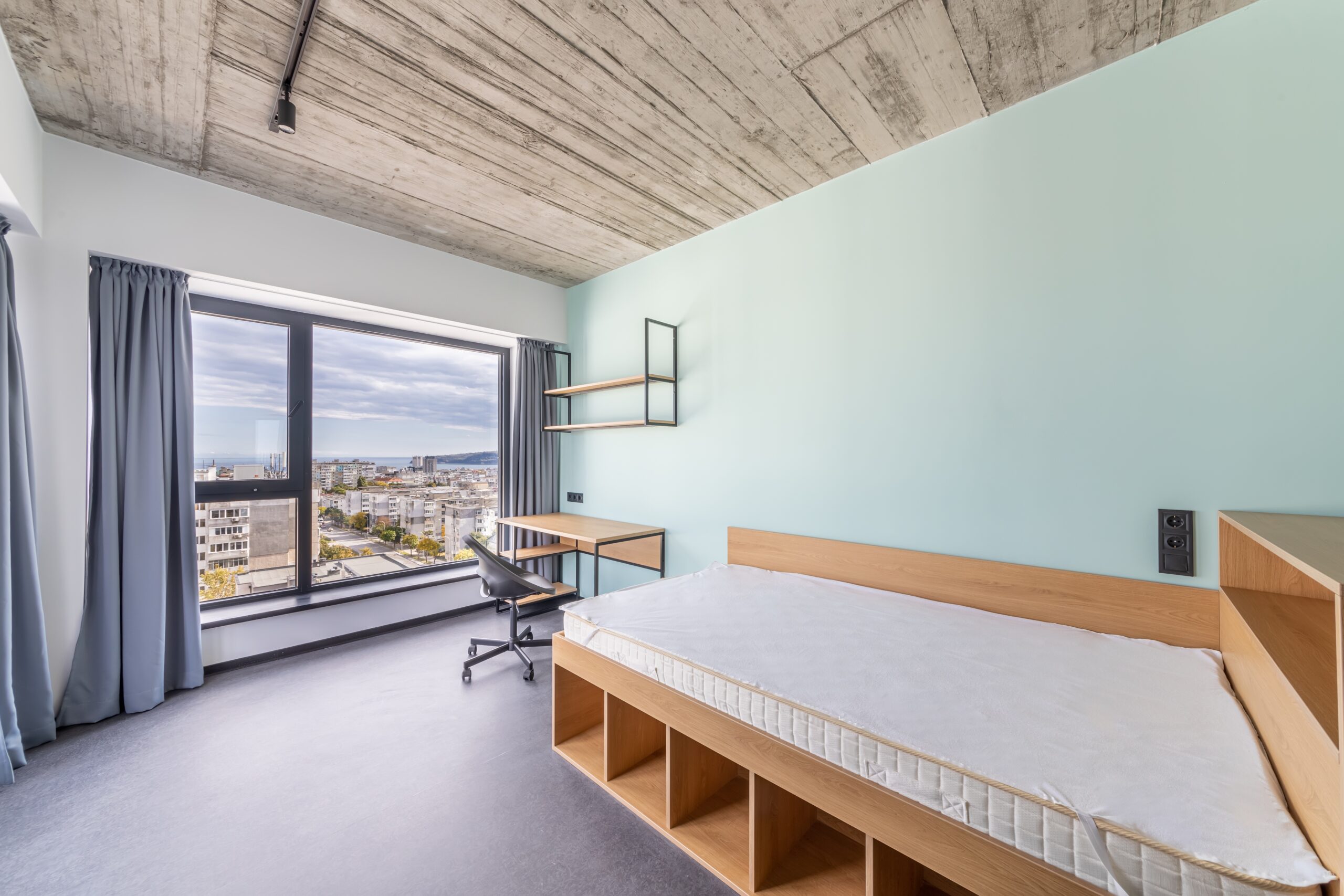 An image of university student accomodation with a bed and a large window in the distance.