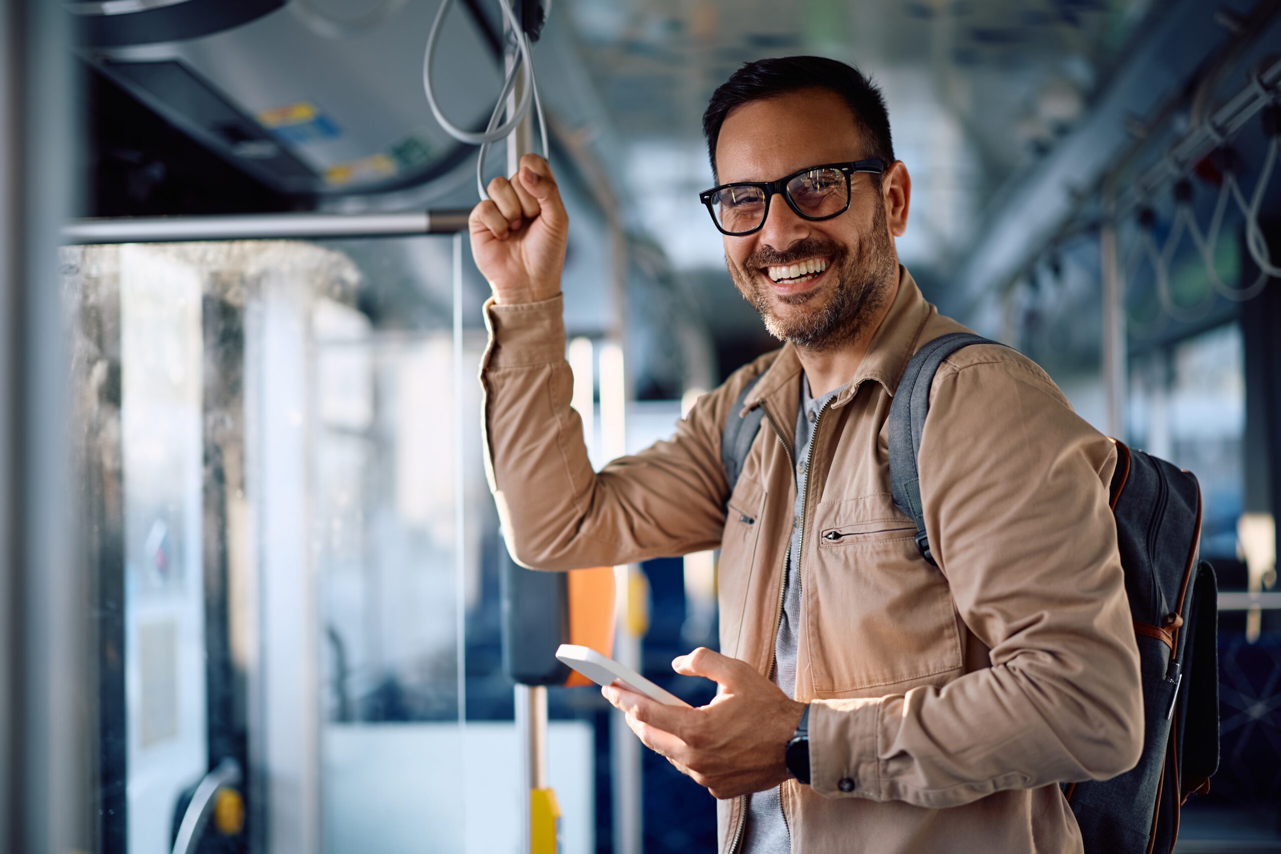 An image of a man smiling and holding onto a handle in a train.