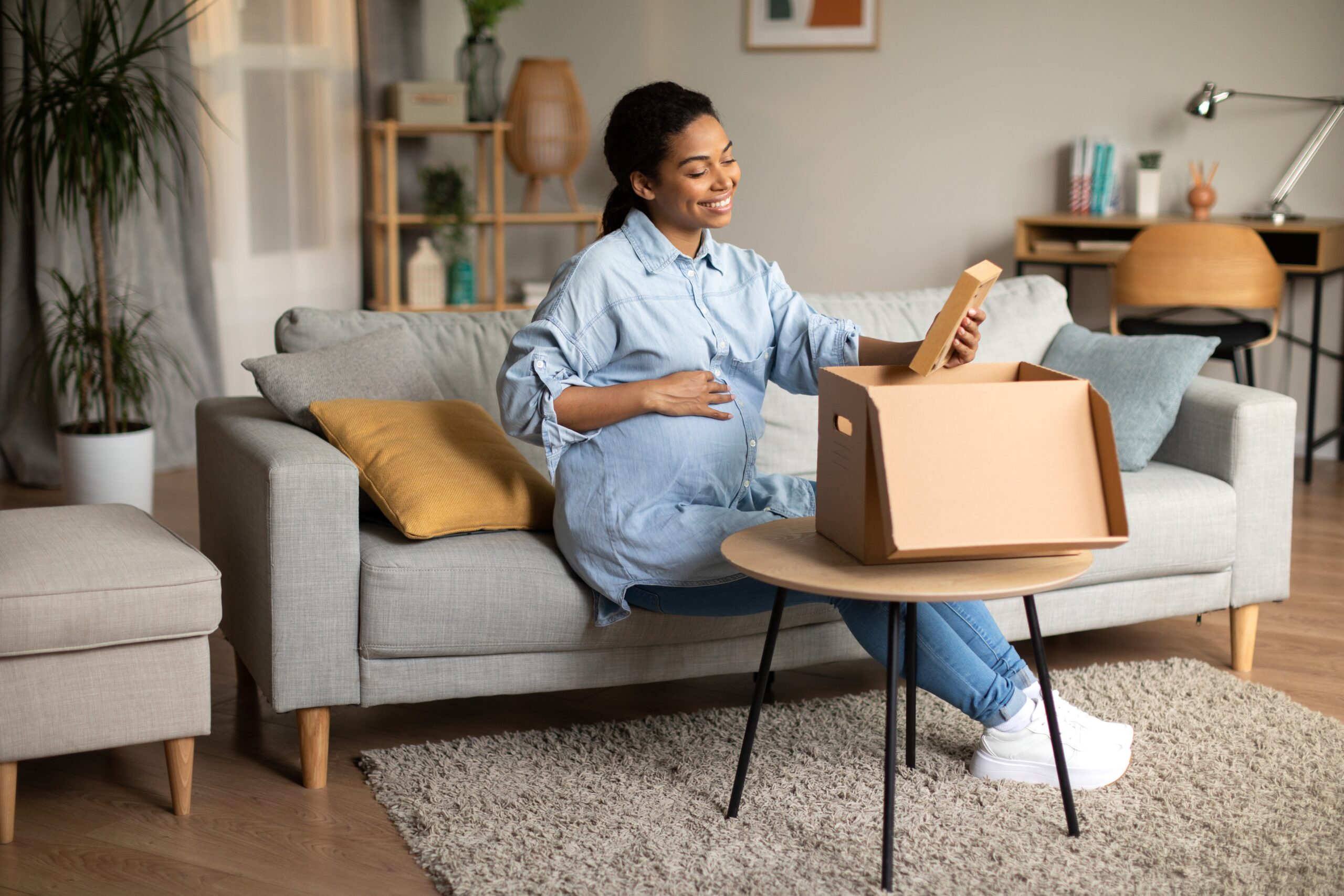 A pregnant woman sat on the sofa sorting through moving boxes and smiling.