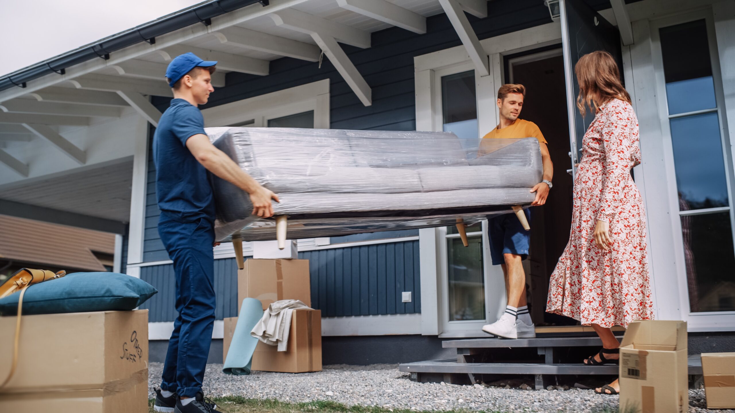 A moving team helping a pregant woman to move house by carrying a sofa through the door.