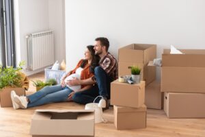 A couple with a pregnant woman sat on the floor with a pile of boxes around them.