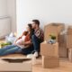 A couple with a pregnant woman sat on the floor with a pile of boxes around them.