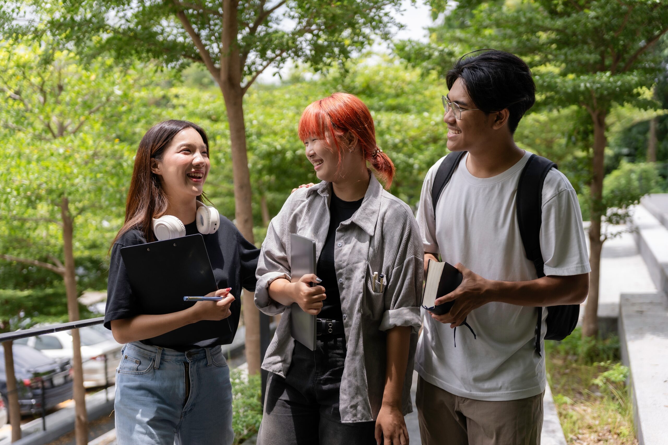 A group of three students all smiling and talking together outside.