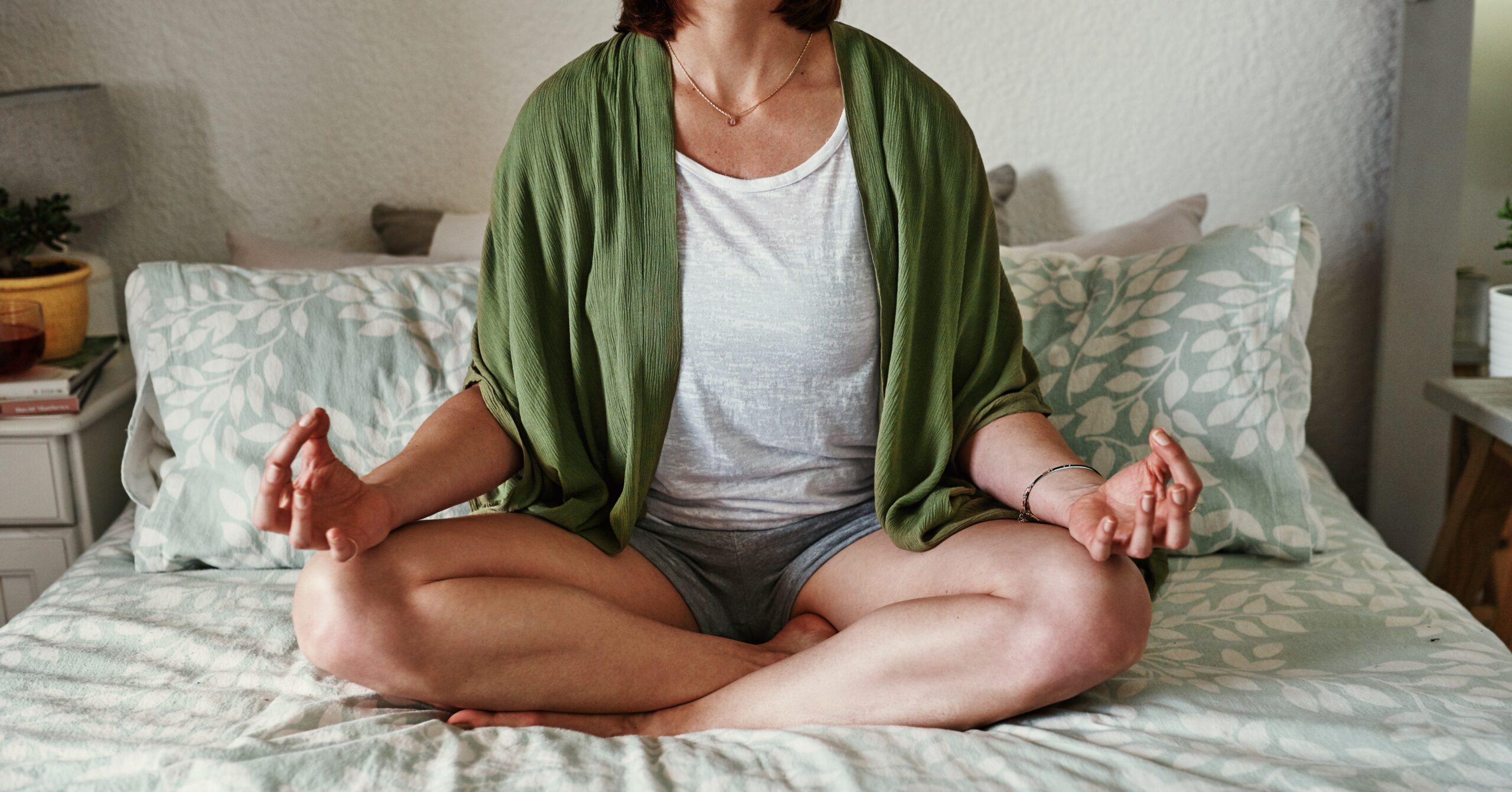 An image of a woman meditating on her bed.
