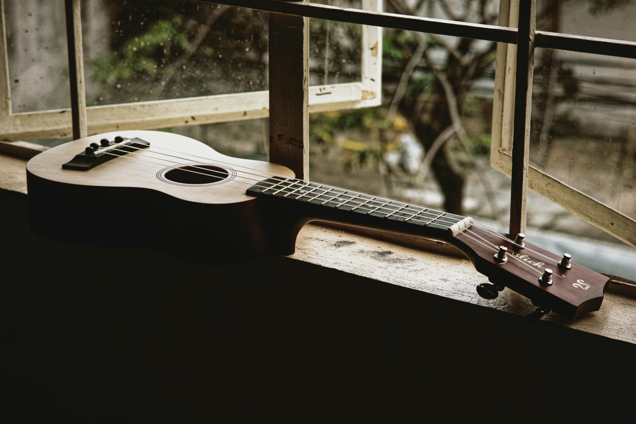 A ukulele laying on a window ledge inside a house.
